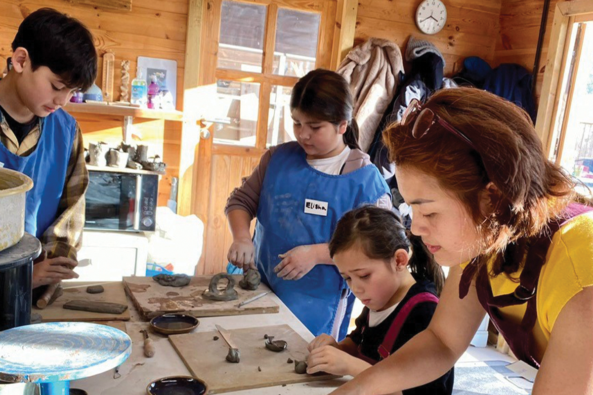 Three children and one adult making models with clay.  All are wearing aprons. 
